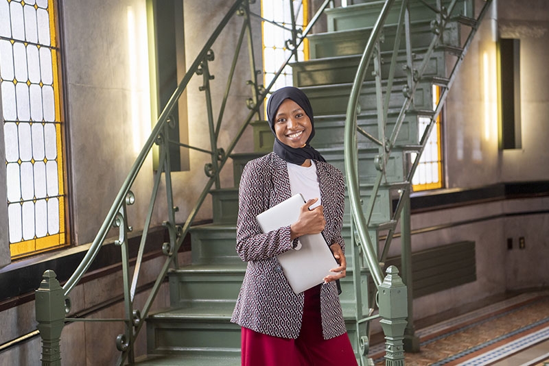  A student holding a laptop poses at the bottom of the Nott Memorial's interior staircase