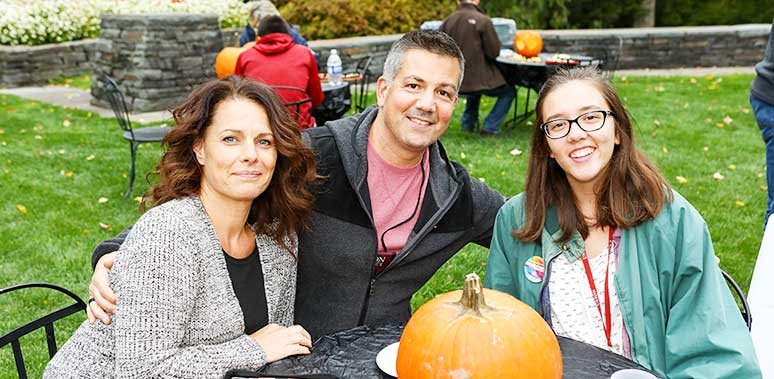 A family at Homecoming pose with a pumpkin.