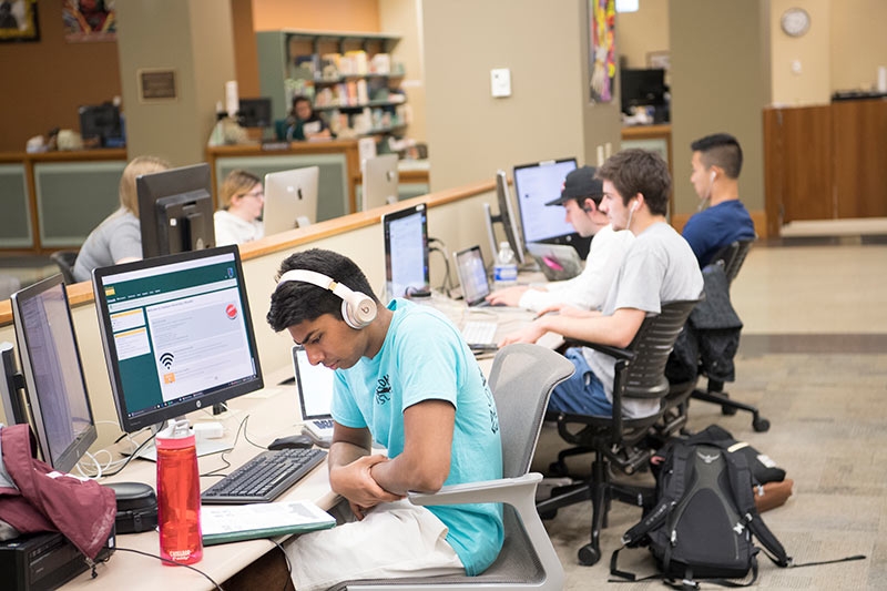 A student wearing headphones listens to instructional materials in a multimedia learning area within Schaffer Librar