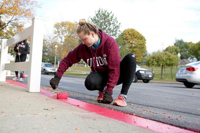 A student participant in Toll Day paints a curb.