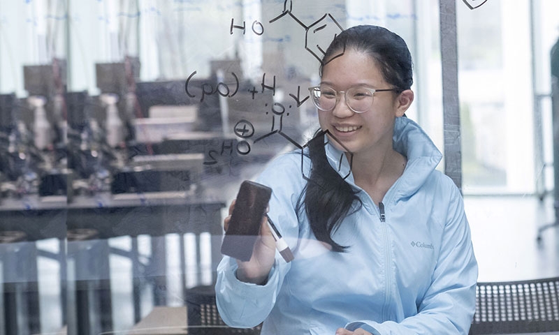 A student writes equation on a window