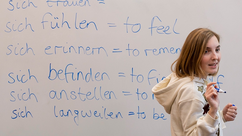 A students stands in front of a whiteboard with German writing on it.