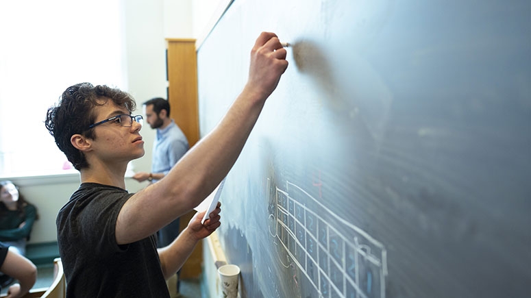 A student writes mathematic equations on a chalk board