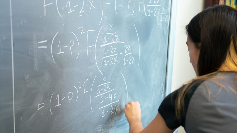 A student writes equations on a chalk board