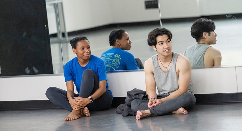 Two students in dance attire sit on the floor of the elegant Henle Dance Pavilion, taking a break from their routine.