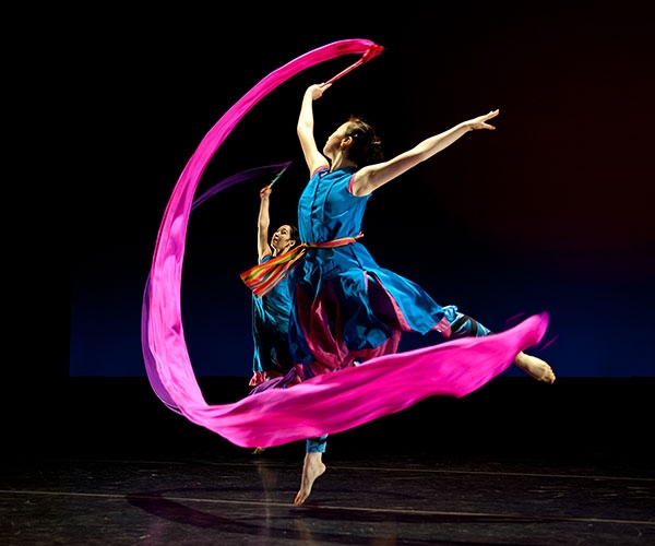 A dancer with a very long. pink piece of fabric that she is twirling