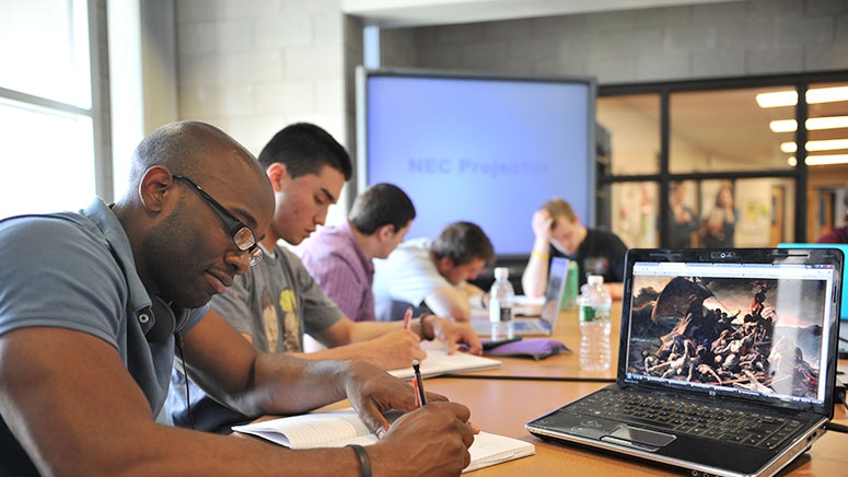 A student takes notes as he watches a movie ion a monitor in a film studies class