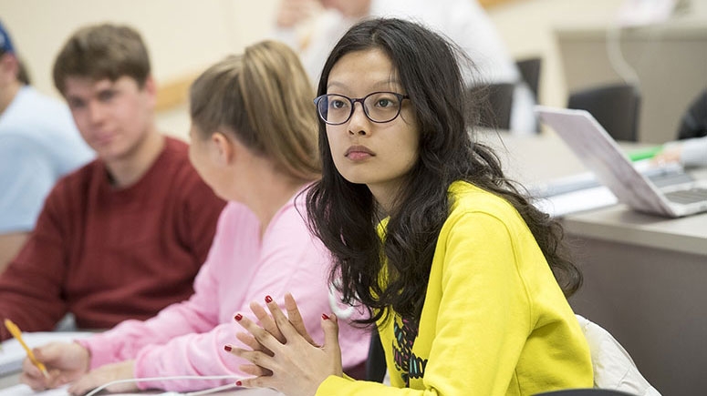 A group of students in a classroom attentively listening to the instructor.