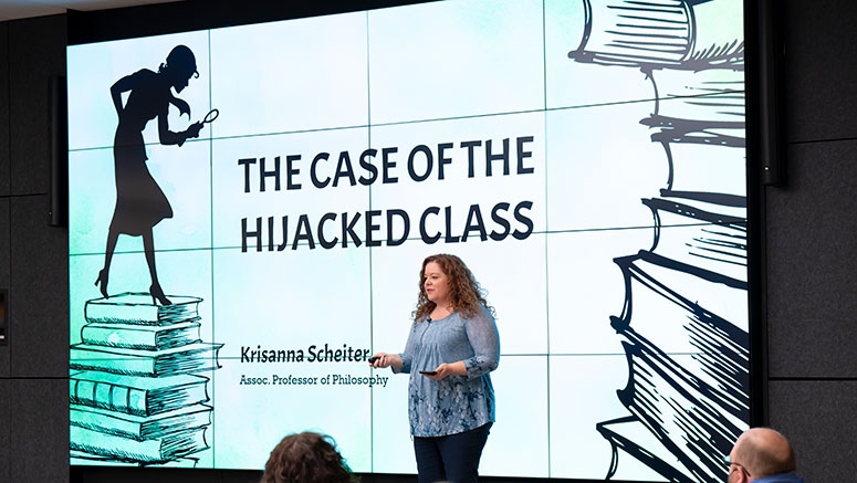 A professor stands at the front of a lecture hall, gesturing while presenting a slide titled "The Case of the Hijacked Class."