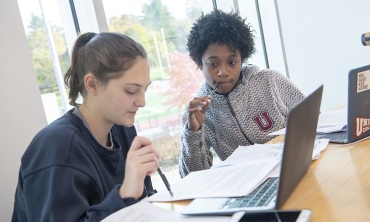 Students in a biology classroom conducting research together while viewing information on a laptop screen.