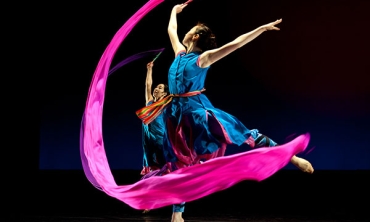 A dancer with a very long. pink piece of fabric that she is twirling